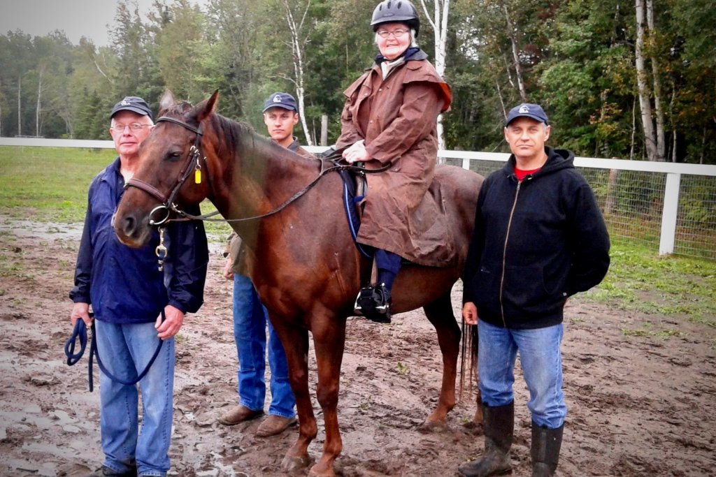 A woman on a horse with instructors standing on each side of the horse, everyones posing for the photo by looking at the camera