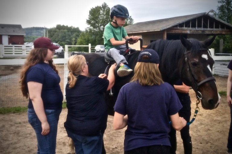 A child on a horse with three instructors supervising the situation.