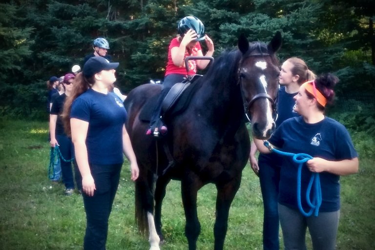 People surrounding a child on a horse and are assisting the child with any uncertainties.