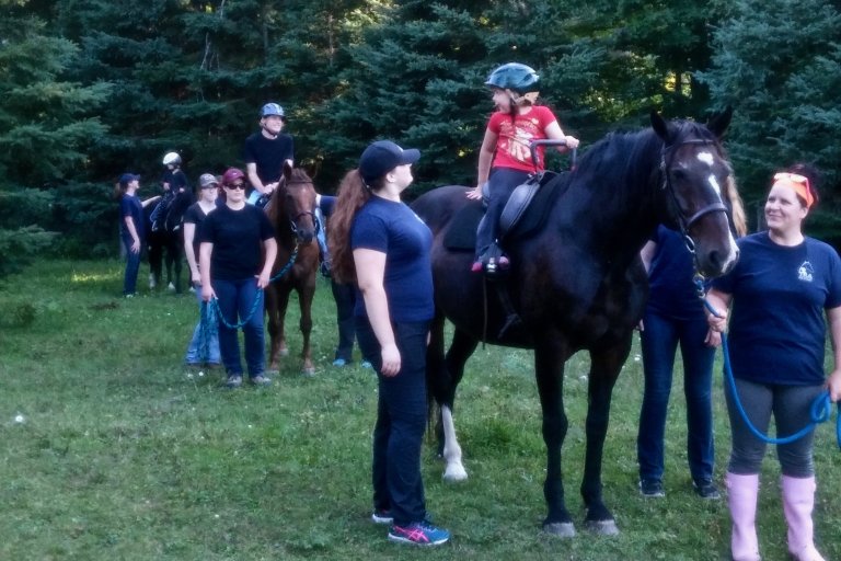 Shows a group of riding students, being lead by instructors. 2 lessons seem to be happening in the current scene.